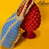 L'immagine mostra una borsa azzurra all'uncinetto con strisce verticali gialle, dotata di un manico coordinato e una chiusura magnetica. Sogno Mediterraneo: il fascino del mare nella tua mano.